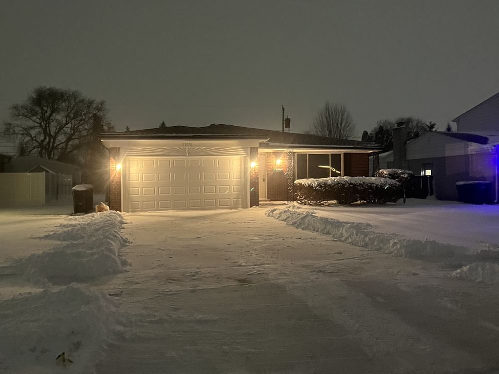 A plowed residential driveway lit up during a night snowfall